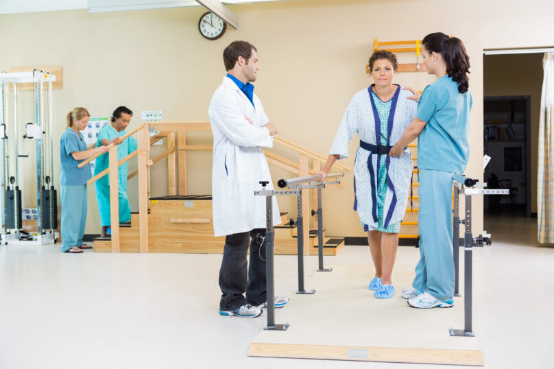 Physical therapists assisting female patient in walking with the support of handrails